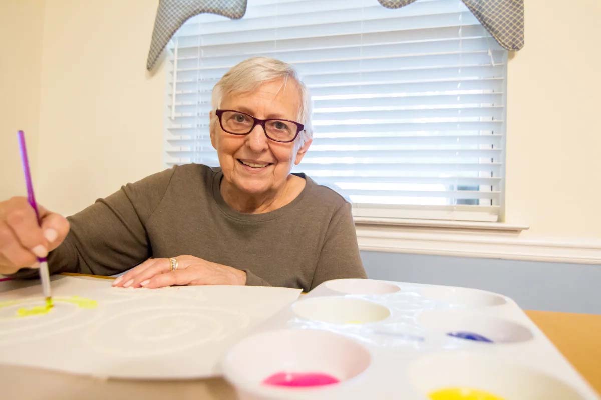 Elderly woman painting with watercolors, smiling happily indoors.
