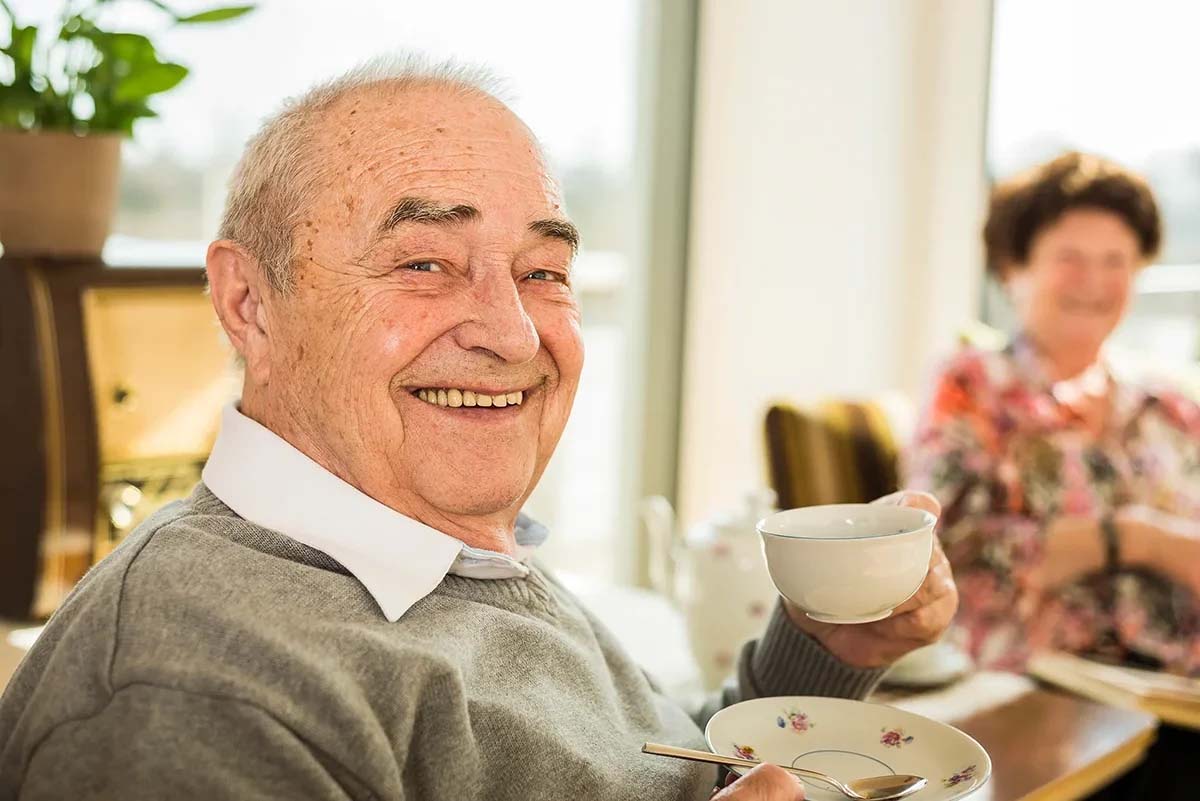 Smiling elderly man holding a cup, enjoying tea time.